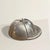 At first glance, it’s a polished little keepsake — a vintage English silver-plate jockey’s helmet, gleaming softly on the...