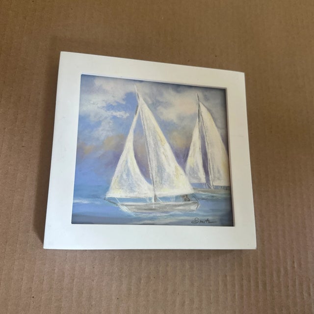 Framed in crisp white, this nautical watercolor shows two graceful sailboats gliding under soft clouds—a bright and airy...
