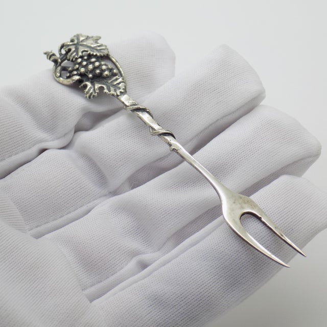 An elegant vintage cocktail fork featuring a grape cluster motif, crafted in Arezzo between the 1990s and early 2000s in...
