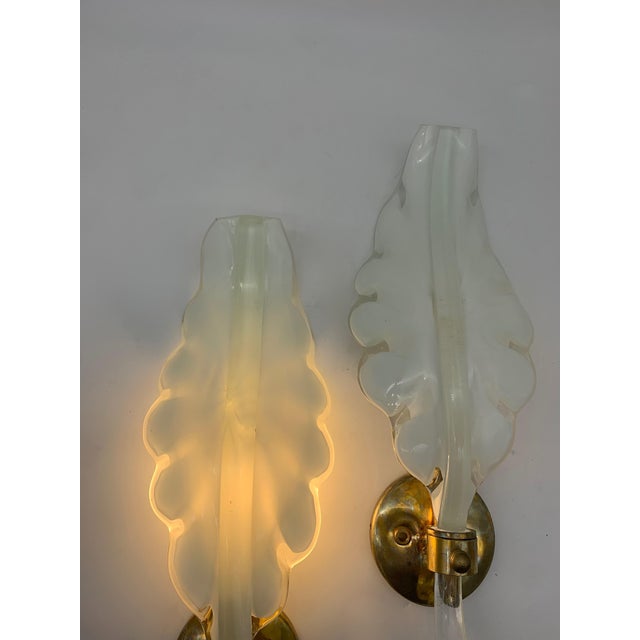 A similar pair of wall sconces crafted from blown milky glass with a stylized leaf shape, characterized by soft lines and...