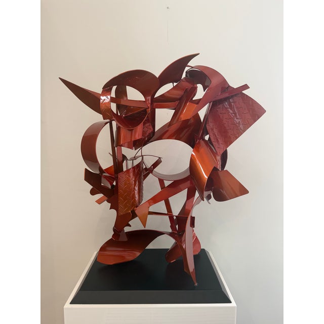 A dynamic abstract steel sculpture in high-gloss crimson, combining industrial textures with sweeping geometric forms to...