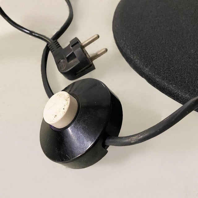 Floor lamp with black metal stem structure with a round cast iron base with a rough finish and an elongated, curved matte...