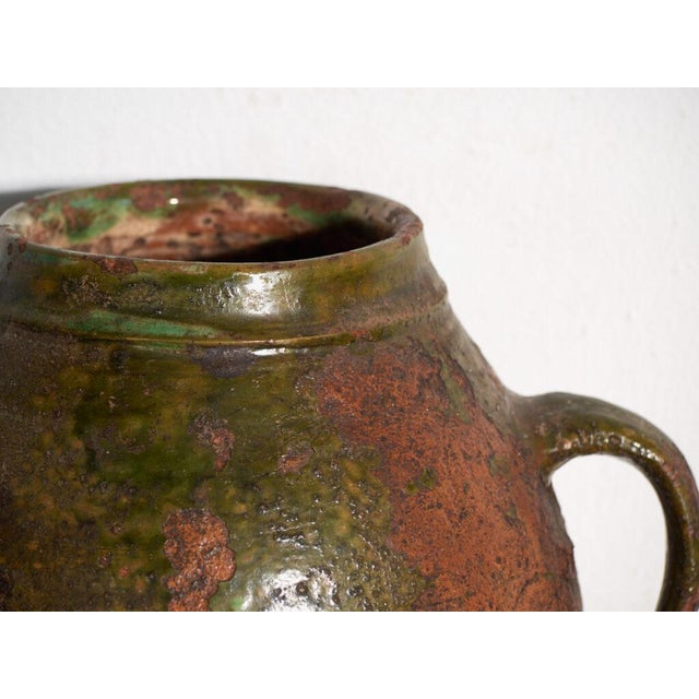 This antique two-handled glazed earthenware pot is a terracotta vessel covered with a green lead glaze. It originates from...