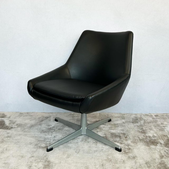 Swivel armchair with bucket seat construction and wraparound back. The molded seat shell is upholstered in black vinyl...
