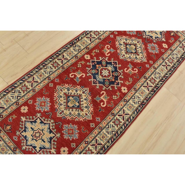 A tribal Caucasian Kazak runner hand-knotted with fine wool on a cotton foundation. This rug features geometric medallions...