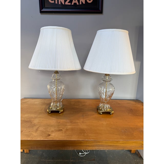 Beautiful vintage pair of Hollywood Regency style cut crystal and brass table lamps with white pleated silk shades. The...