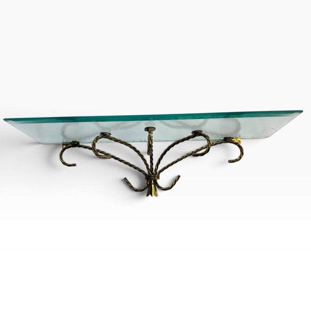 Striking vintage Hollywood Regency wall shelf featuring a clear glass shelf with a subtle aqua-green edge, supported by an...