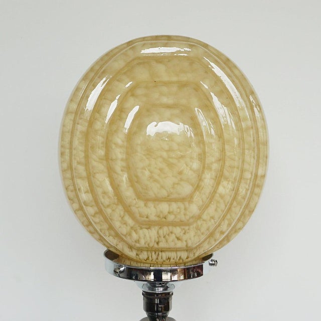 An Art Deco table lamp. Reeded bakelite stem with an impressive sized mottled glass shade, set over a circular chromed...