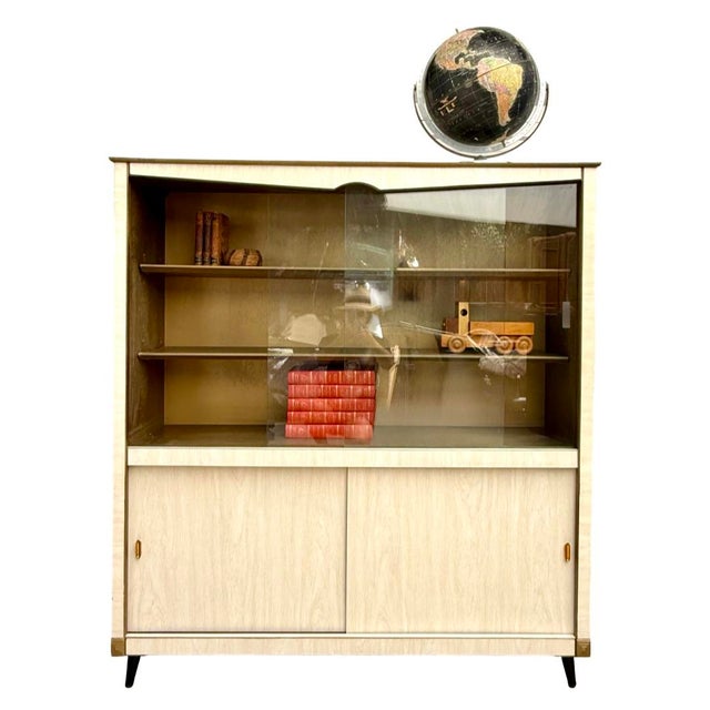 Here is a stylish mid-century modern display cabinet featuring a cream faux bois laminate accented by delicate woodgrain...