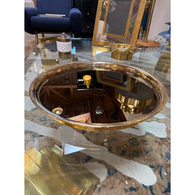 Elegant Italian serving tray featuring a round smoked-glass surface framed by a polished brass rim. Its clean, minimalist...