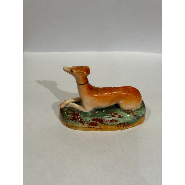 This is a 19th Century, Victorian era antique Staffordshire porcelain figurine. It depicts a greyhound lying down. It is...