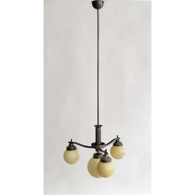Elegant Art Deco chandelier made of silver-colored metal with buttercream-colored glass orbs, in good condition with light...