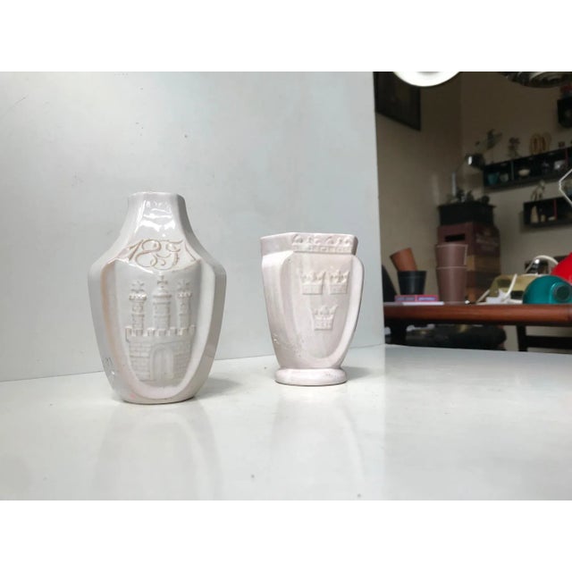 A set of pottery vases in delicate white glaze revealing the red clay underneath. Both decorated with relief motifs. One...