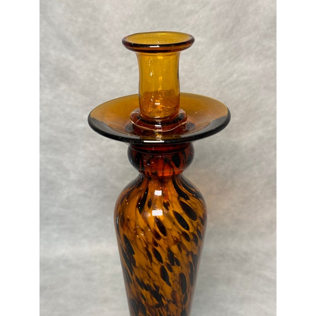 Slender candlestick made of hand-blown art glass in amber tones with a decorative dark pattern. The sculptural form and...
