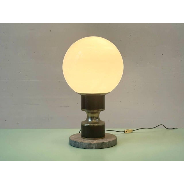 A striking table lamp from Italy, featuring a heavy marble base, a sculptural metal stem with a brass finish, and a large...