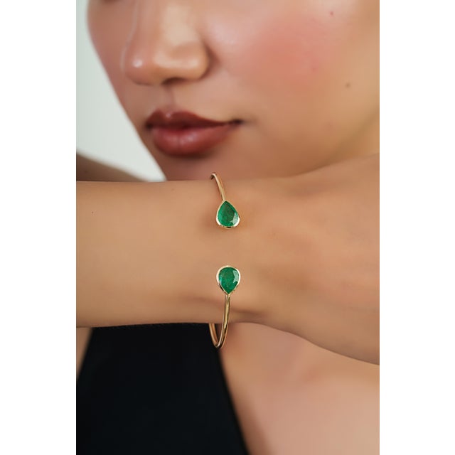 This open cuff bangle bracelet features 2.58 carats of pear-shaped emeralds, Crafted in 14K yellow gold. Each emerald...