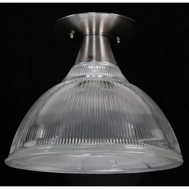 Industrial style flush mount featuring a clear prismatic Holophane shade paired with a bottom lens and a brushed steel...