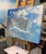 This painting features a dynamic sky, where swirling clouds interact with vibrant blue hues, creating a sense of movement...