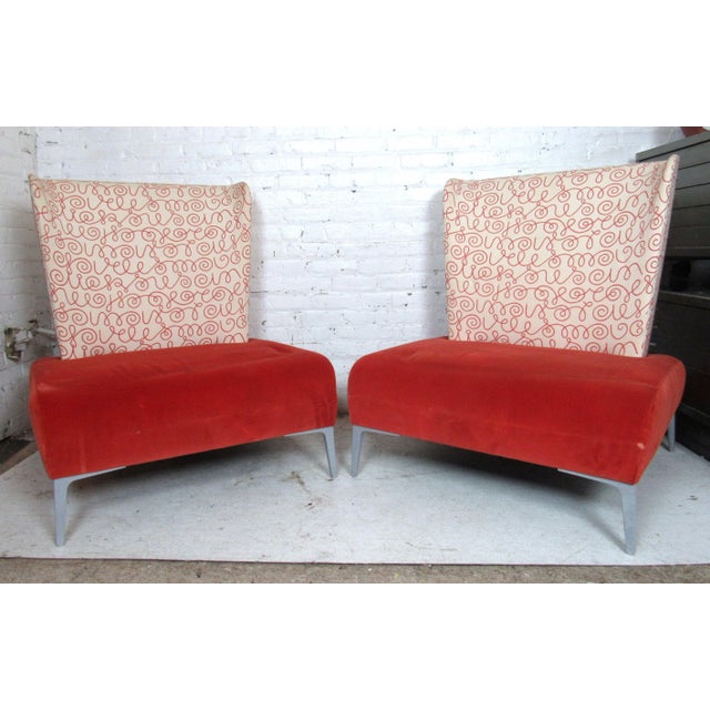 Mid-century style lounge chairs featuring a uniquely designed backrest, large red comfortable seat, on a set of sturdy...