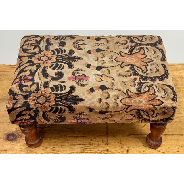 Antique footstool with brocade-style floral fabric to upper deck and turned wood legs. Rectangular in shape and sturdy.