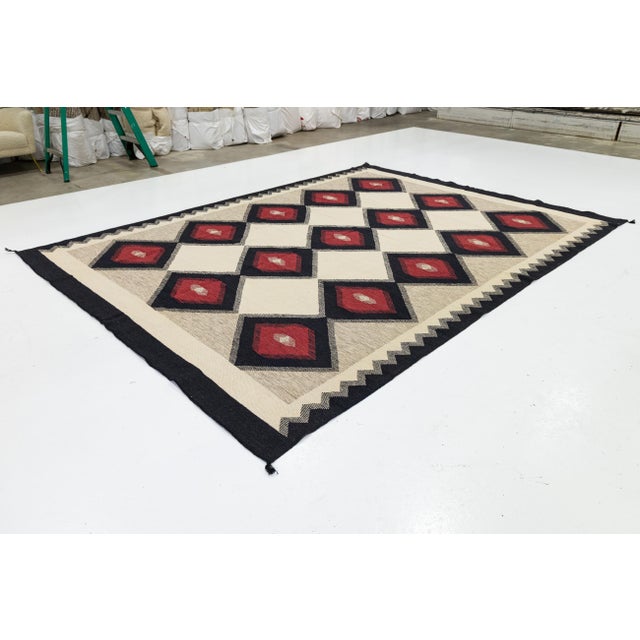 This striking handmade rug features a bold Navajo-inspired aesthetic, blending traditional Southwestern motifs with a...