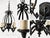 This chandelier features a sculptural black wrought-iron frame with elegant scrollwork, candle-style holders, and a...