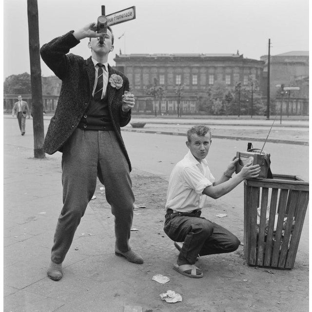 East Berlin May Day 1961 View of two young men, one drinking from a bottle and the other tuning a portable radio, on the...