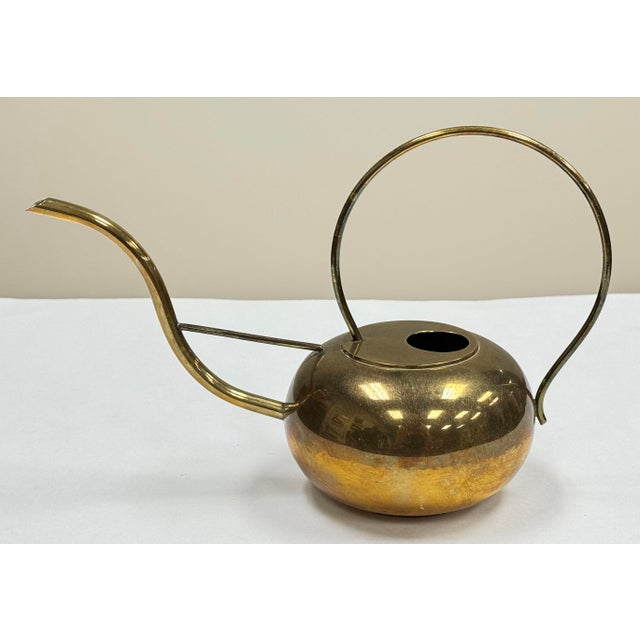 Vintage sculptural brass watering can. Sophisticated curved leg attaches to rounded body with domed handle. Marked to...
