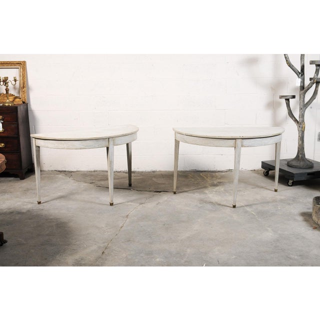 This elegant pair of French demi-lune consoles features a beautifully restrained white painted finish accented by delicate...