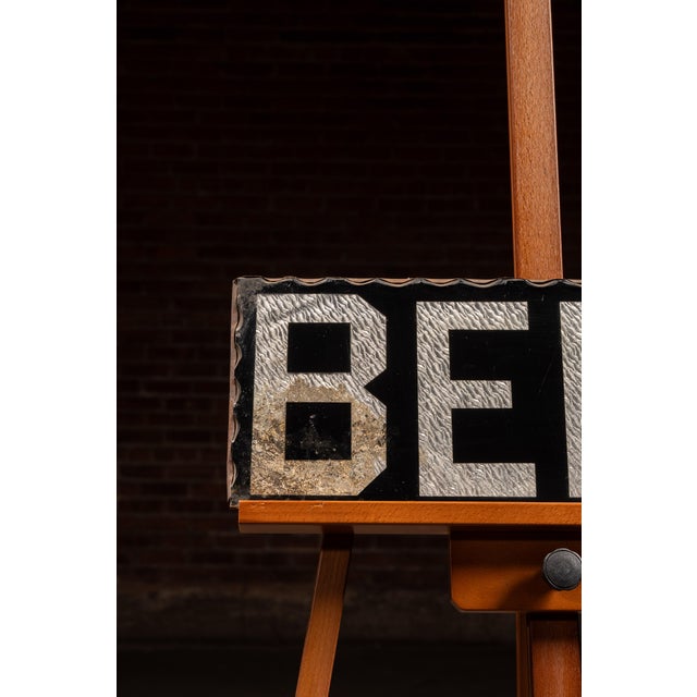 Reverse foil on glass advertising sign featuring bold block "BEER" lettering rendered in black over a textured silver foil...