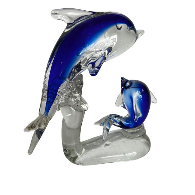 The object is a handblown art glass sculpture of two dolphins - an adult leaping upward and a smaller dolphin beside it,...