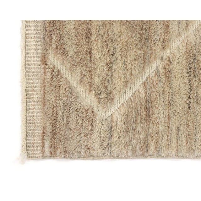 Luxuriously hand-knotted wool rug displaying a distinctive pattern with diamond motifs transitioning into an abstract,...