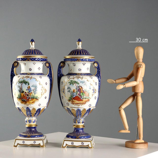 A pair of Sèvres porcelain lidded vases with gold and cobalt blue decorations. The vase's belly features a scene with...