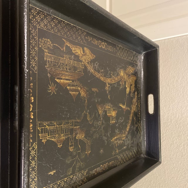 A classic Hollywood Regency-style butler’s tray table featuring a hand-painted gilt landscape on a "Japanned" black...