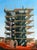This oil painting depicts a towering construction site, with workers navigating the scaffolding against a bright blue sky....