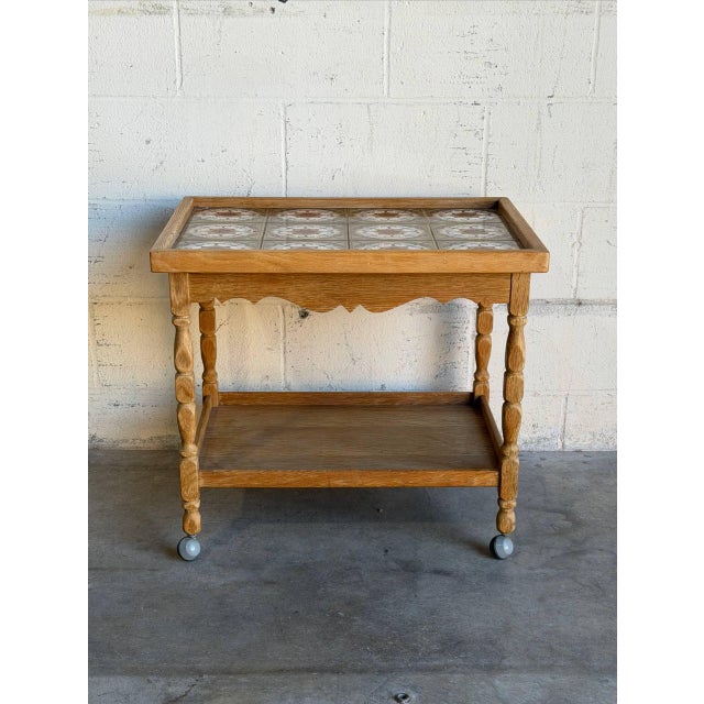 This vintage serving tea table features a striking tile inlay top paired with traditionally sculpted legs. The dynamic...