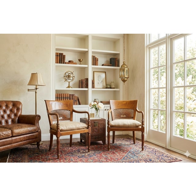 A handsome pair of Anglo-Indian style armchairs crafted in warm honey-toned hardwood, featuring gracefully scrolled open...