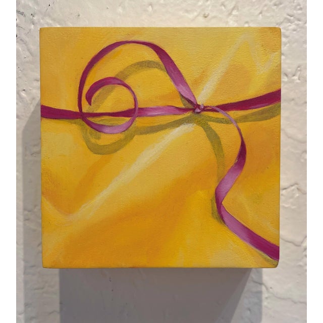 This artwork features a vibrant gold gift box tied with a delicate pink ribbon, set against a warm yellow background. The...