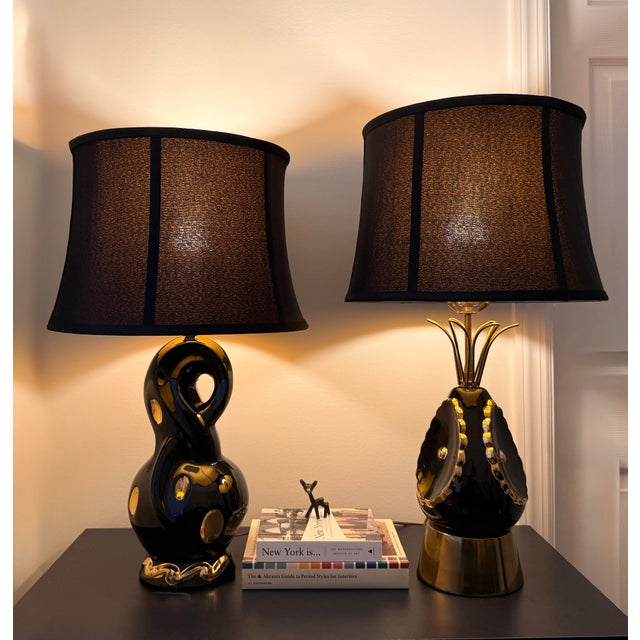 A striking companion pair of vintage sculptural ceramic table lamps in glossy black glaze with warm gilt accents and...