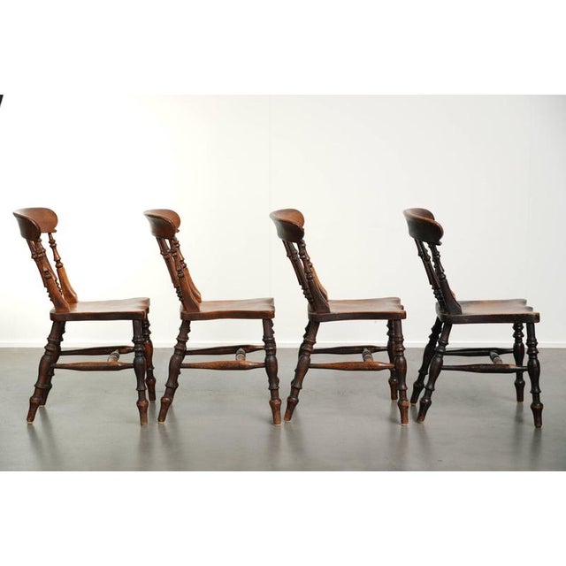 This exceptional set of 4 antique English wooden Windsor farm chairs features a unique design and beautiful colors. A...