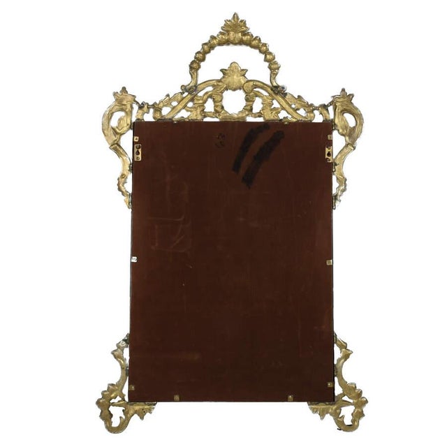 A Large Ornate French Brass Wall Mirror features an intricate brass frame with elaborate details like floral patterns and...
