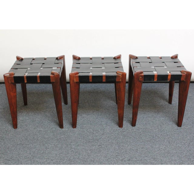 Sculptural teak wood stools with laced leather seats by Edmond Spence. Solid teak frames retain their original dark stain,...