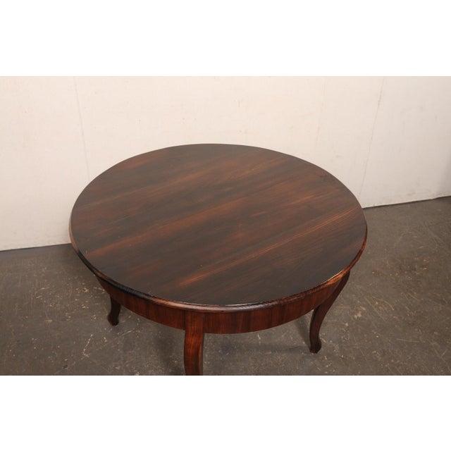 A French Provincial 45.75" round wooden table from the mid 20th century. This vintage table from France, crafted from...