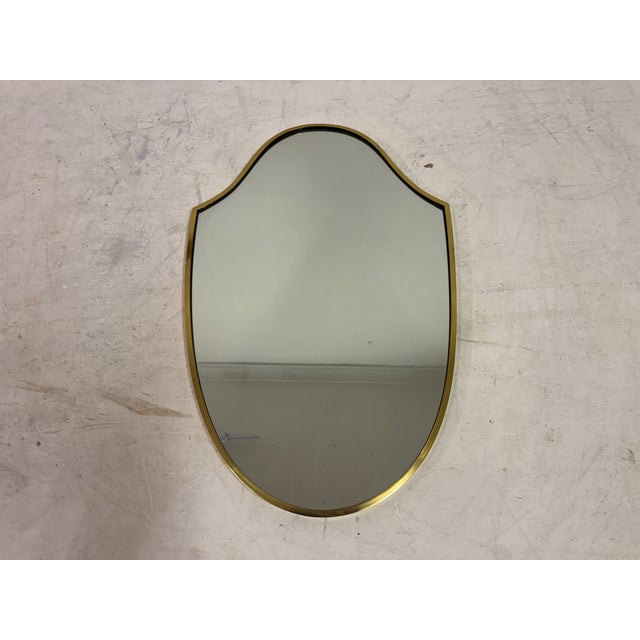 An Italian brass wall mirror, circa 1970s. The mirror is defined by its softly contoured, shield-like form, with gently...