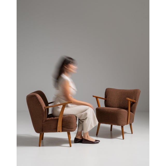 This pair of 1940s Mid-Century Modern upholstered armchairs from Denmark, covered in warm brown bouclé with slim, honey-...