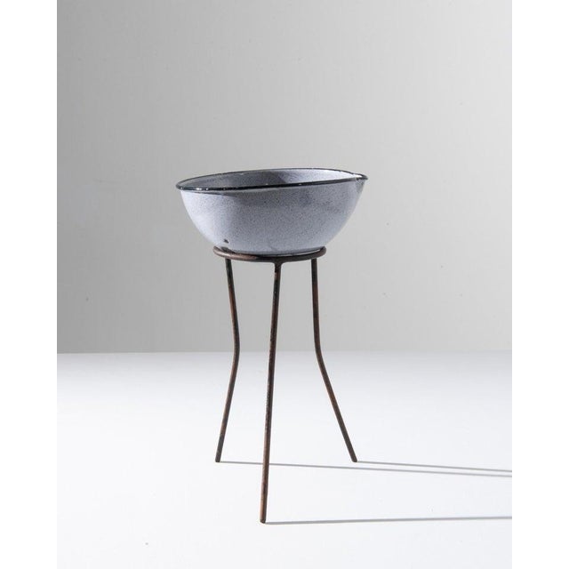 A 20th century enameled bowl on stand from Central Europe, this small antique wash basin elevates upon oxidized metal...