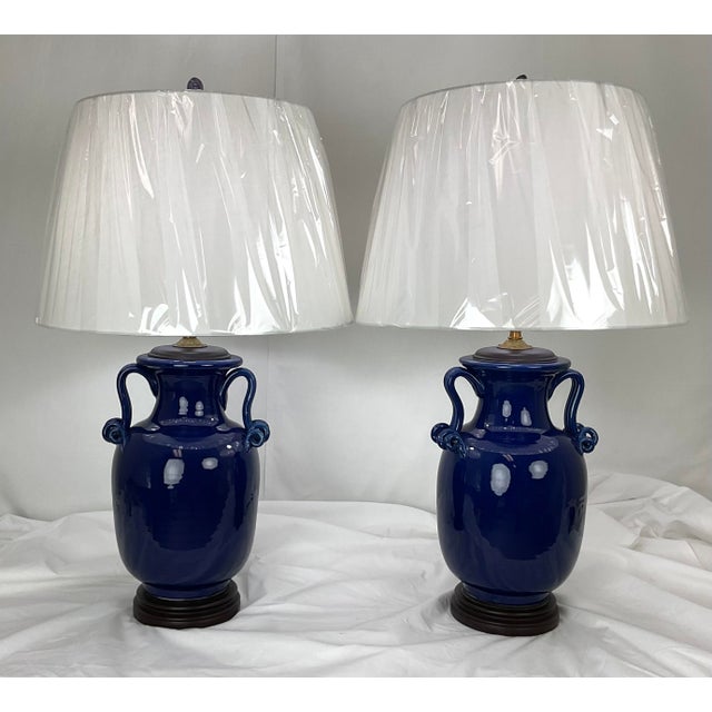 An elegant pair of substantial porcelain urn-form table lamps finished in a rich, glossy cobalt blue glaze. Each lamp...
