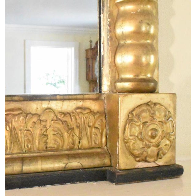A substantial American Empire overmantle mirror, Circa 1800 to 1830s. The overhang cornice is enriched with floral detail...