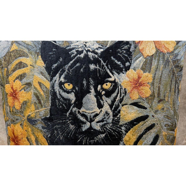 A black panther stares directly forward from a field of tropical leaves and orange hibiscus, its yellow eyes the only warm...