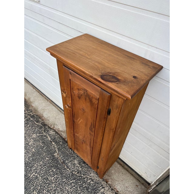 This antique freestanding storage cabinet features knotty pine construction, beveled door with wooden pull and latch, and...